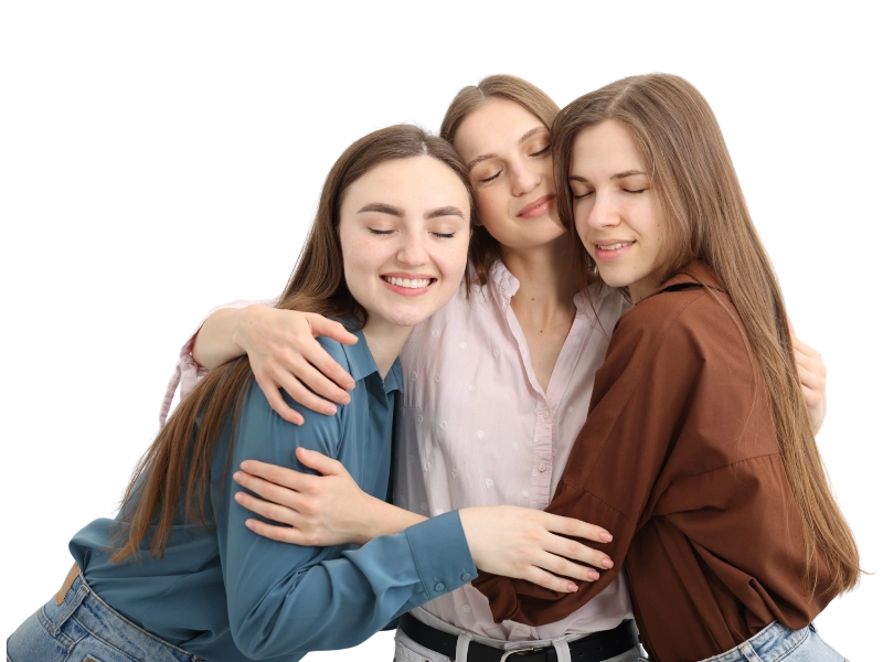 Three women embrace each other warmly against a solid black background, conveying friendship and support.