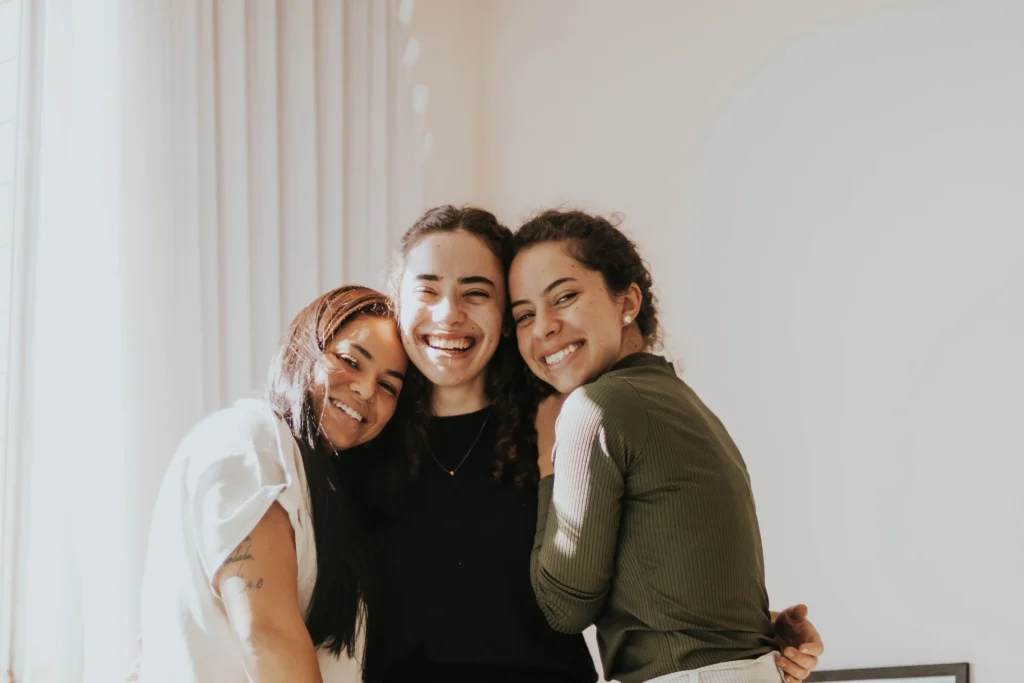 sober living community Woodland Hills Three women embrace each other warmly in a cozy room, showcasing friendship and support.