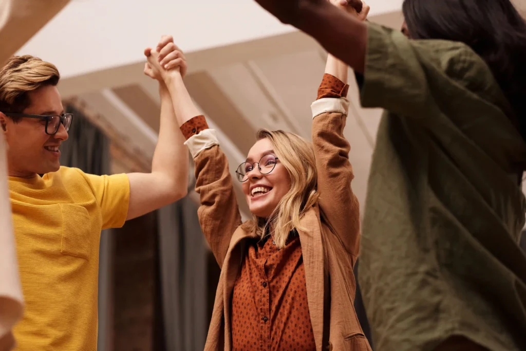 Sober Living Programs & Services. Three individuals standing together, holding hands in a supportive group gesture. Sober Living Programs & Services